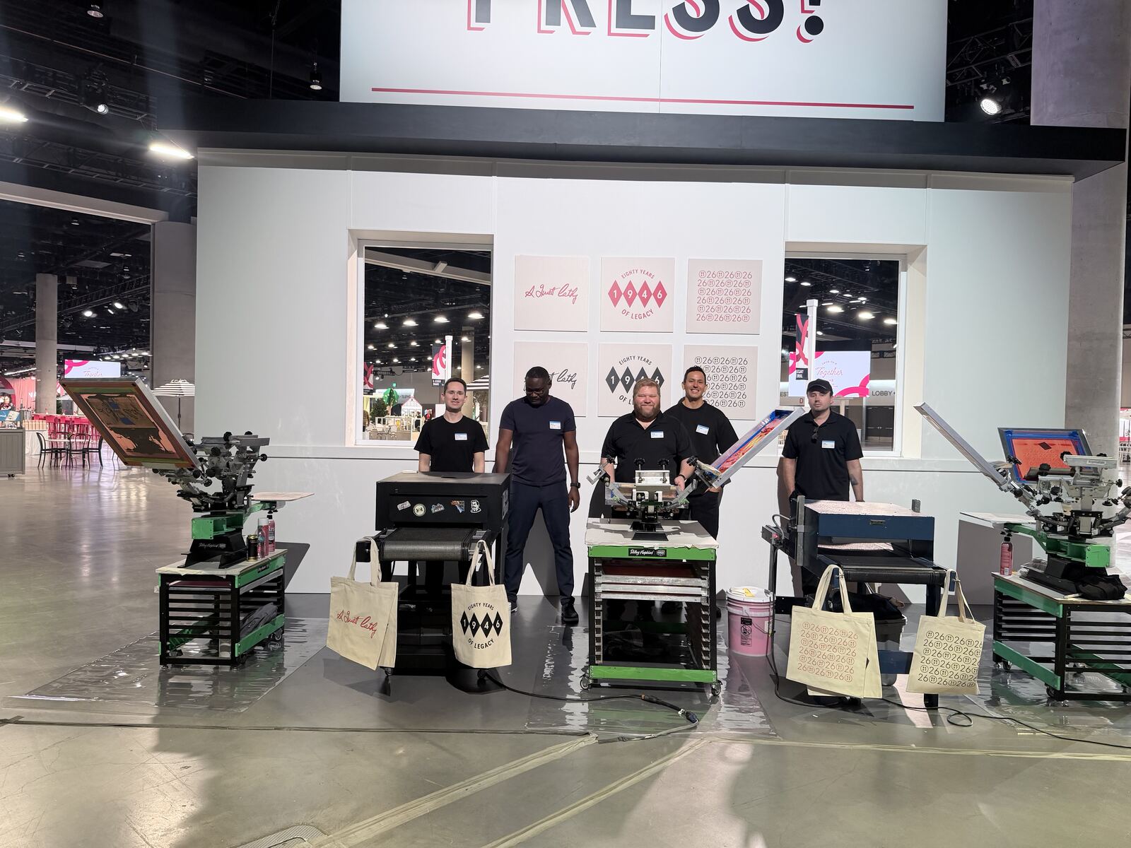 Live printing demonstration with multiple decorated t-shirts displayed overhead and attendees watching the production process